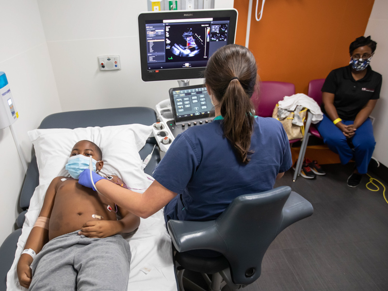 Recovering from MIS-C, Xavier Gardner gets an echocardiogram from sonographer Chasity Robertson as his mother, Cheryl Gardner, looks on.