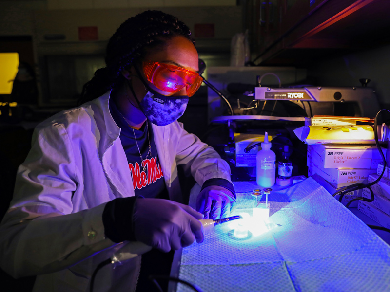Nena Hawkins using a dental light curing unit to activate a dual-cured resin cement through an all-ceramic sample that later will be laser irradiated and tested to determine bond strength test.