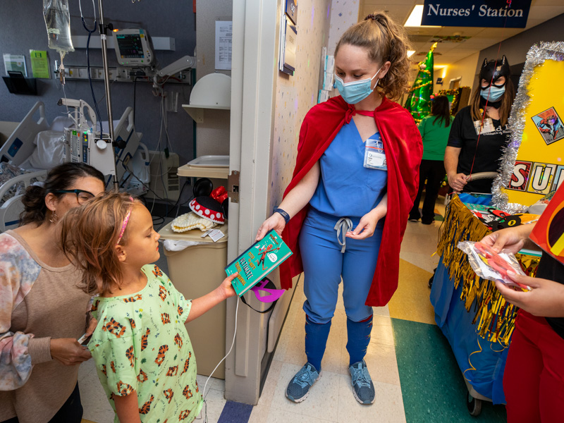 Medical student Marilyn Pigott, dressed as a superhero, presents Children's of Mississippi patient Eden Crews of Pelahatchie a book during the children's hospital's Thanksgiving Parade Nov. 22.