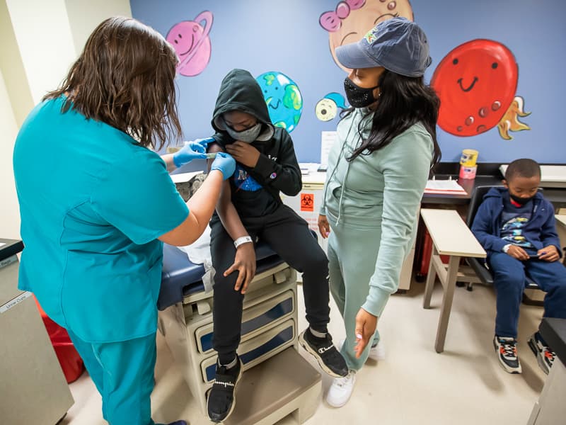 Zenus Marshall of Jackson, with mom Shelearria Gaylor beside him, watches as nurse manager Kristen Cherry places a bandage on his arm after COVID-19 vaccination.