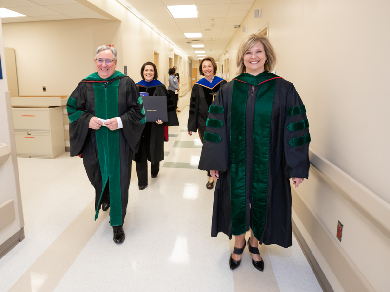 Didlake, left, joins Dr. LouAnn Woodward, right foreground, and, from left, background, Dr. Kristi Moore, chair of the Department of Clinical and Diagnostic Sciences in the School of Health Related Professions (SHRP); and Dr. Jessica Bailey, dean of SHRP, on their way to a bedside graduation ceremony for SHRP student Sarah Herrington in May 2019.