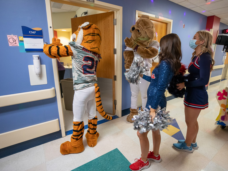 Waving at a Children's of Mississippi patient are Sonny Thee Tiger of Jackson State, Bully of Mississippi STate, Ole Miss dance team member Jane Granberry and Ole Miss cheerleader Mara Liston, right. Jay Ferchaud/ UMMC Communications