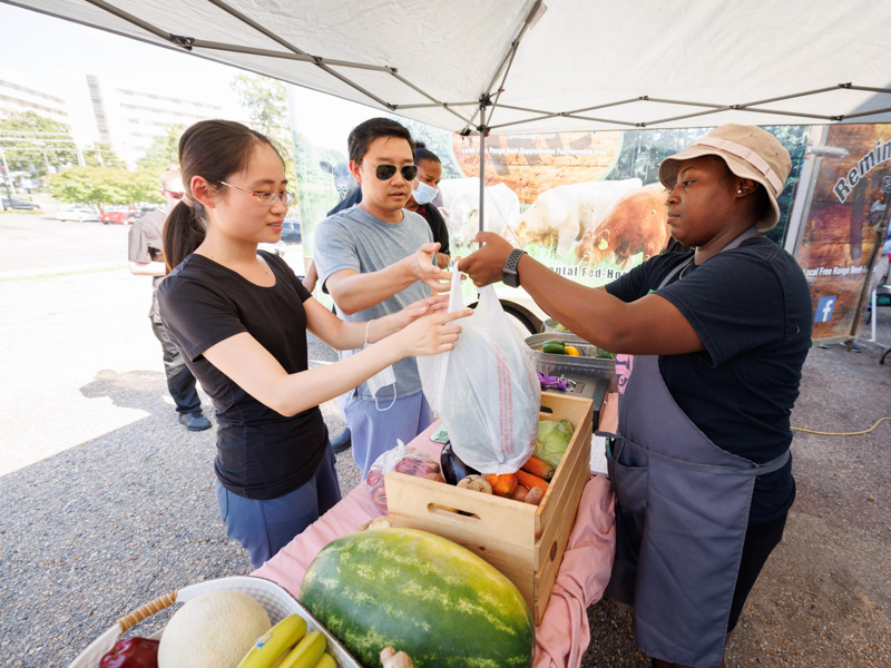 Rui Xu, left, a researcher in the Department of Physiology and Biophysics, and her husband Xiaochen He, a postdoctoral research fellow in the same department, buy fresh produce from Michel'le Wheatley of Foot Print Farms at Thursday afternoon's Farmer's Market behind Backyard Burger. The event was sponsored by the UMMC Office of Well-being. Joe Ellis/ UMMC Communications 