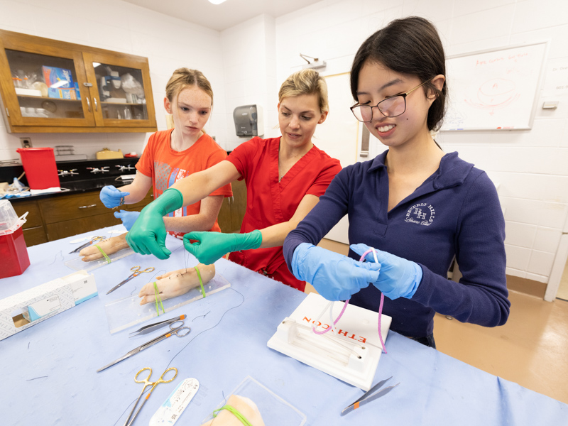 Emma Rhodes, left of Kosciusko High School, and Rachael Ni of Carthage, right, are instructed in suturing and knot-tying techniques by Shelley Edwards, a UMMC MD/PhD student. Jay Ferchaud/ UMMC Communications 