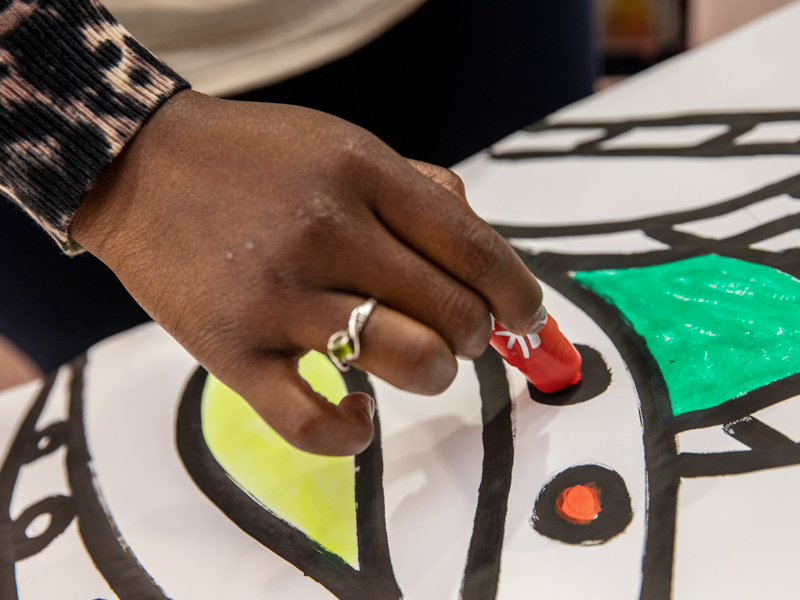 Employees and students use paint sticks to add their contributions to a collaborative art project that will hang in the hospital.