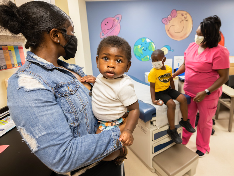 Markerria Mays holds brother Olliver Shaw, 8 months, before his COVID-19 vaccination. Olliver's older brother Omari, beside mother Kanyatice Shaw, got his vaccination first.  Melanie Thortis/ UMMC Communications