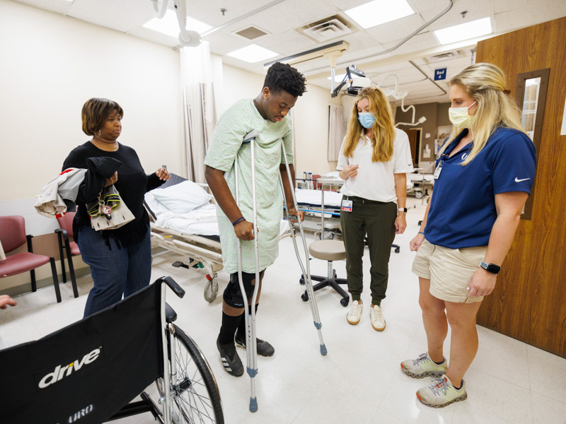 Sports medicine fellow Dr. Laura Fincher, second from right, and Ashlyn Mendrop, a sports medicine physical therapy resident, fit Brian Washington with a crutches as Washington's mom, Jacqui Davis, observes. Joe Ellis/ UMMC Communications 