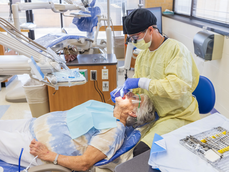 Fourth-year student Hunter Horton cleans the teeth of patient Nelda Yarborough in addition to checking the removable partial denture she wears pending an implant and a crown.