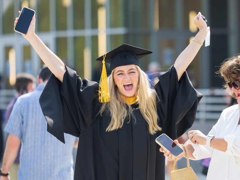 Master of biomedical sciences graduate Cara Irby spots a loved one in the crowd and cheers as her mother, Melanie Irby, prepares to enter the coliseum for commencement. Melanie Thortis/ UMMC Communications 