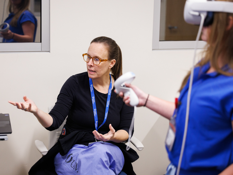 While viewing a computer monitor, SimGym creator Dr. Emily Tarver explains some of the highlights of her VR simulation software to medical student Chappel Pettit.