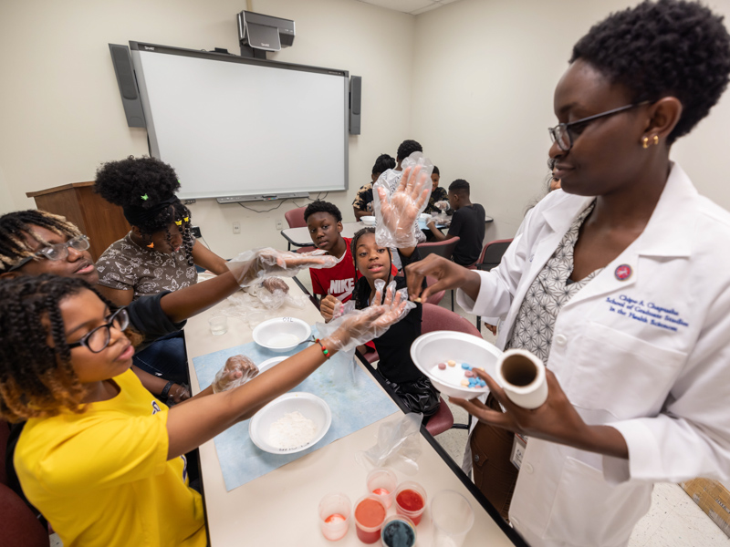 School of Graduate Studies in the Health Sciences PhD student Chipo Chapusha leads an activity to test medicine release rates with middle schoolers, clockwise from left, De'Nahri Middleton, Aiden Wynn, Kyndal Lewis, Connor Harrell and Journi Garvis.