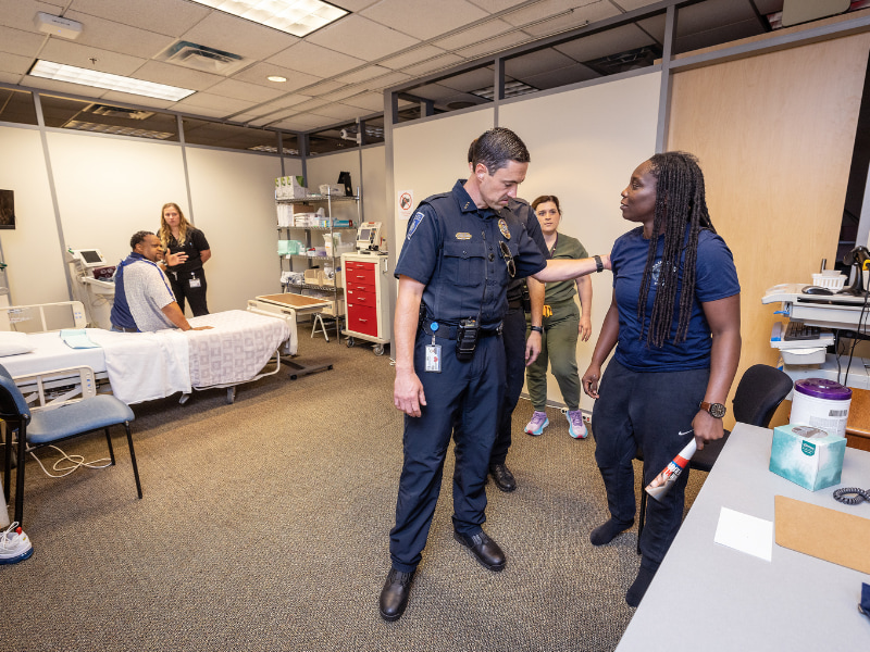 After Accelerated BSN students Melody Kneezel, center, and Sarah Keaton Odom, left, called for police during a simulation, Deputy Chief of Police Joshua Bromen talks with officer Shanice Mays.