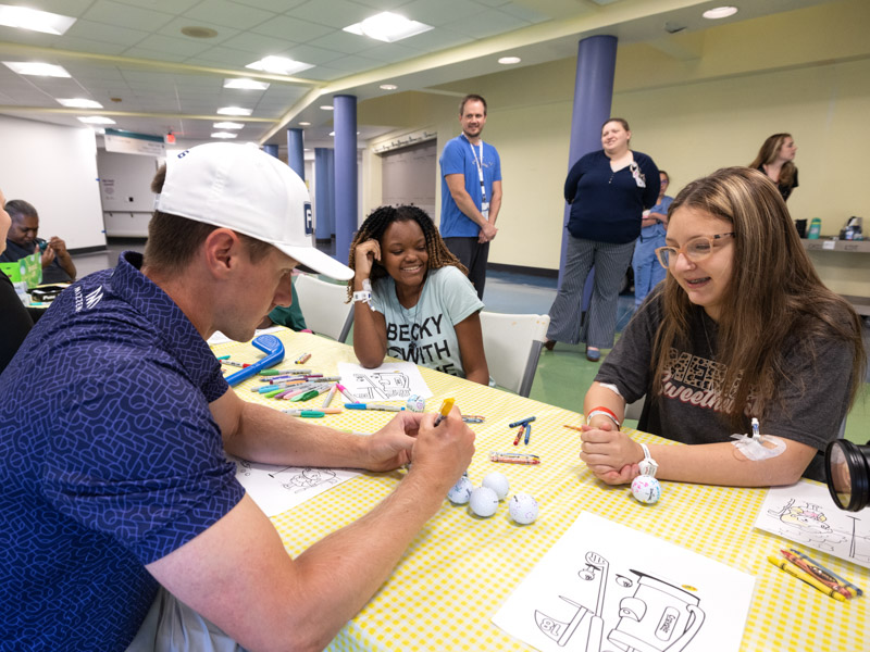 2022 Sanderson Farms Championship winner Mackenzie Hughes decorates golf balls with Children's of Mississippi patients Melanie Conner of Clinton and Makayla Jones of Moss Point.