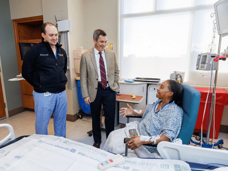 From left, Dr. Nick Derrico, neurosurgery resident, and Dr. Chad Washington, chair of neurosurgery and director of the UMMC Stroke Center, speak with Mabel Bankston the day after her surgery.