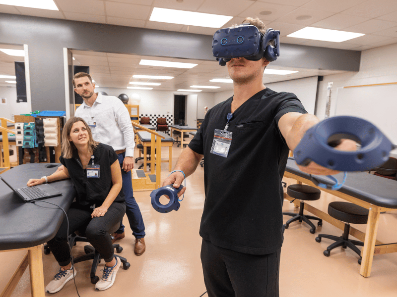 PT student Jacob Lape demonstrates movements used by patients when studied using VR technology as Dr. Jacob Daniels and PT student Abigail Thiessen watch.