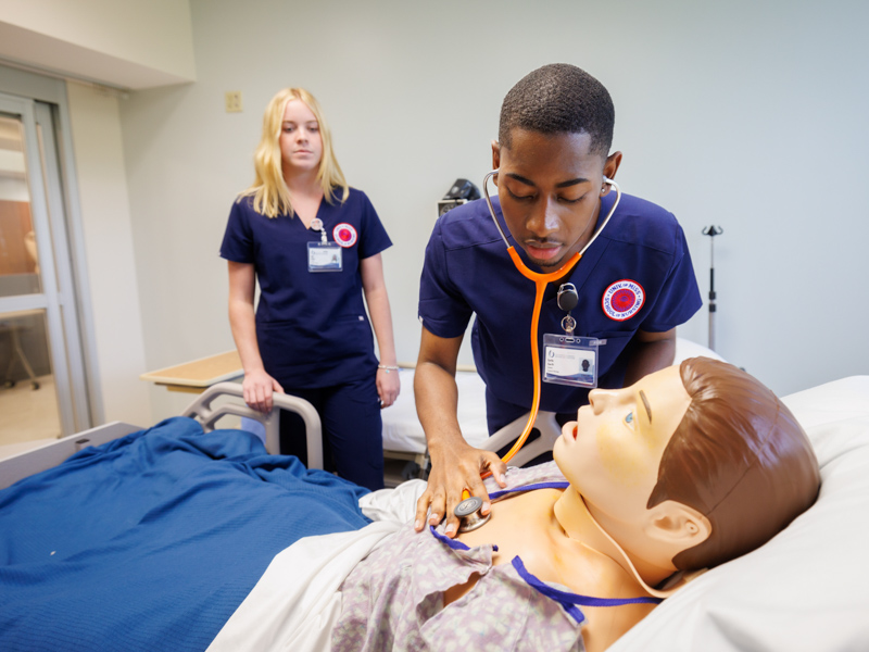 Nursing student Earlie Garth practices taking vital signs in the UMMC School of Nursing's simulation center at the South Oxford Center. Looking on is classmate Allie White.