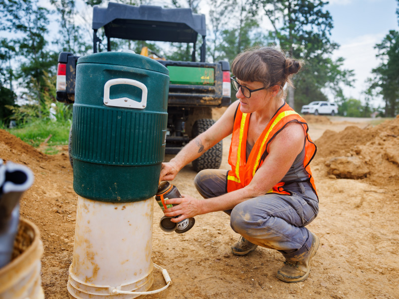 Bioarchaeology Field Technician Emily Wicke stops for a drink of water while working the Asylum Hill Project site on the UMMC Campus.