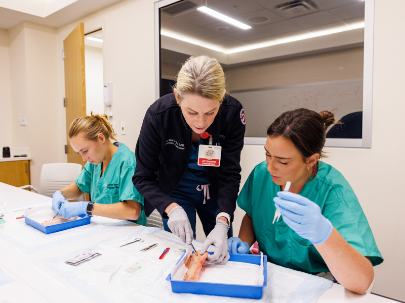 Dr. Risa Moriarty, center, assists new emergency medicine resident, Bethany Fuller, right, with a suturing technique. At work to the left is Lauren Hopper.