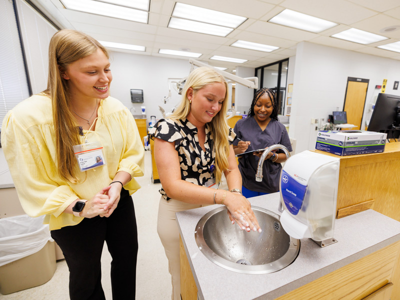 Dental assistant Karis Birden, right, watches incoming dental hygiene student Brooke Anne Renfroe, left, and classmate Magnolia Wingfield during hand washing at School of Dentistry orientation. Jay Ferchaud/ UMMC Communications 