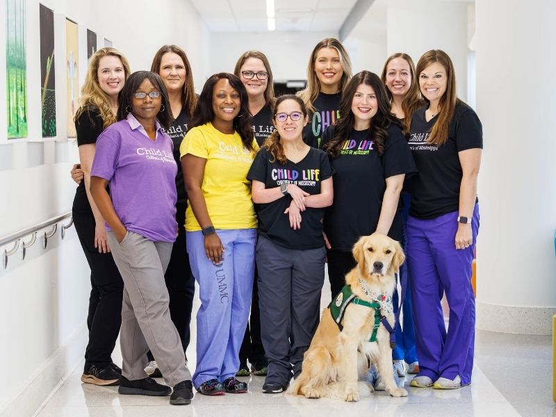 Members of the child life team at Children's of Mississippi include, from left, Madeline Wilson, Michelle Chambers, Pepper Weed-Cooper, Kendra Logan, Ashley Prendez, Avery Friedmann, Allyson Holliman, Kelsey Clark, Claire Humphreys and Cara Williams, manager, with Hollywood. Not pictured is Anne Elizabeth Zegel. Melanie Thortis/ UMMC Communications