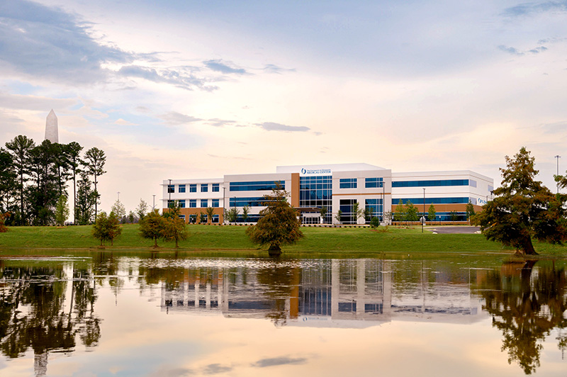 The University of Mississippi Medical Center Colony Park South features a large office building and a tranquil pond in front.