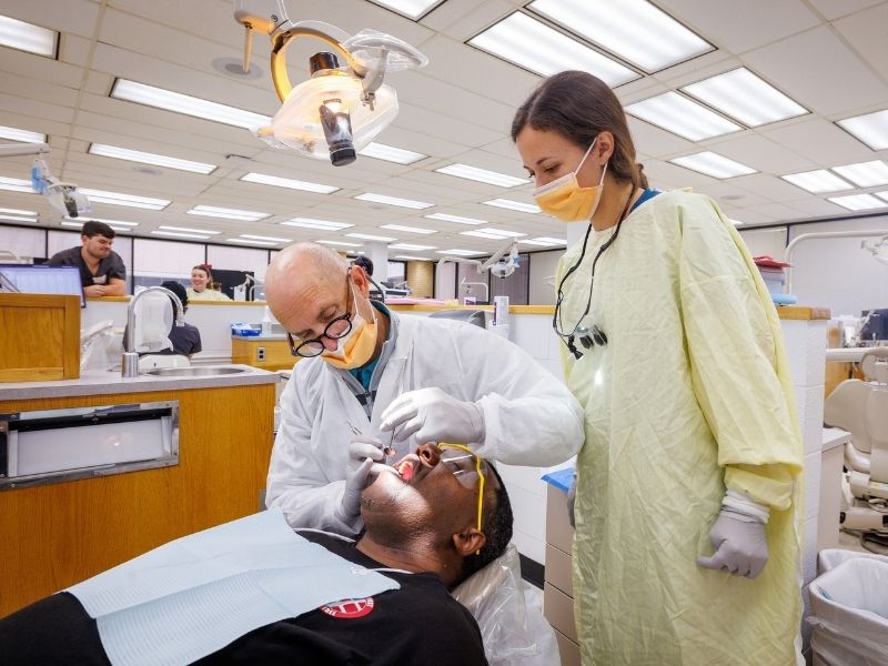 Dr. Michael Fast, director of the Comprehensive General Dentistry Program, and Avery Gibens, third-year dental student, examine patient, Lorenzo Boyland of Pearl, during Dental Mission Week.