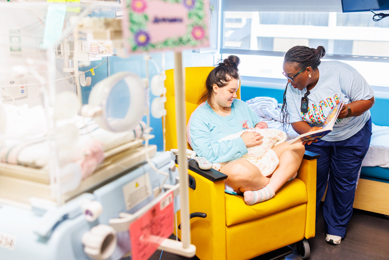 Dr. Mobolaji Famuyide, chief of neonatology, reads to NICU patient Avana Rushing, held by her mother, Isabella Rushing of Wesson.