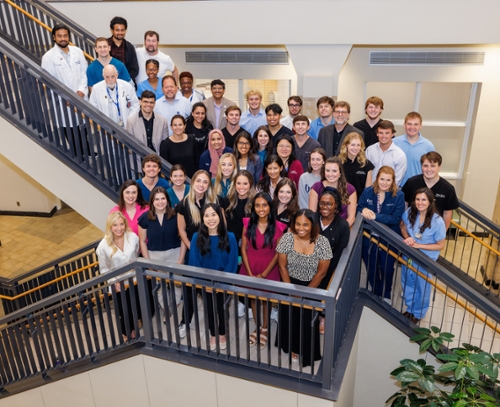 Group picture of UPSTART students and mentors standing at the intersection of two flights of stairs.