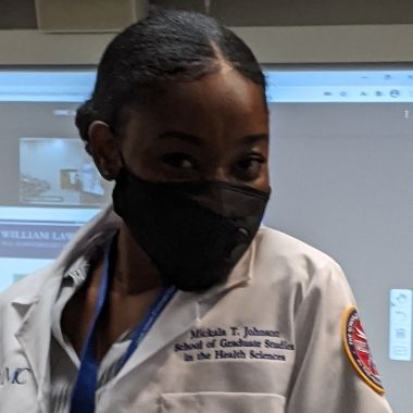 A closeup of a student wearing a mask and showing off her white coat.