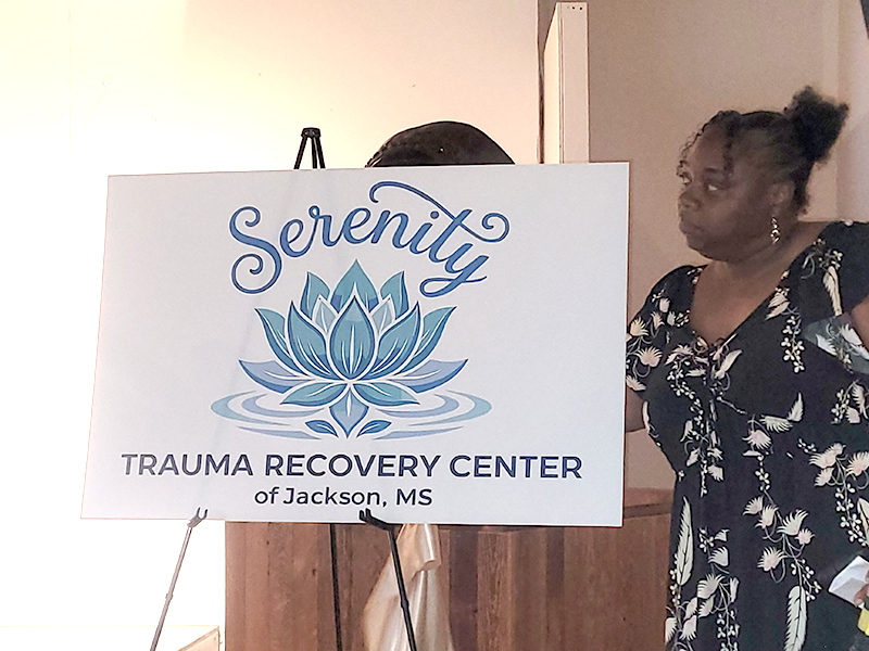 An attendee stands next to the newley-revealed Serenity Trauma Center sign.