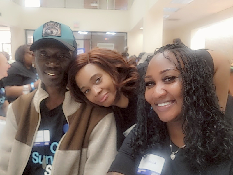 Three participants seated closely indoors at a crowded community meeting wearing Crime Survivors Speak Mississippi shirts.