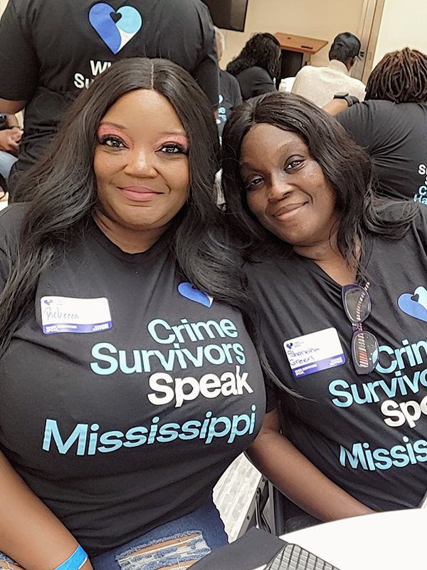 Two participants sitting close together indoors wearing Crime Survivors Speak Mississippi shirts.