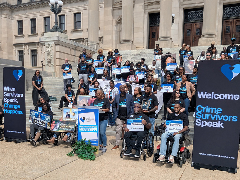 Wide group photo on Capitol steps with banners reading ‘When Survivors Speak, Change Happens’ and ‘Welcome Crime Survivors Speak.’
