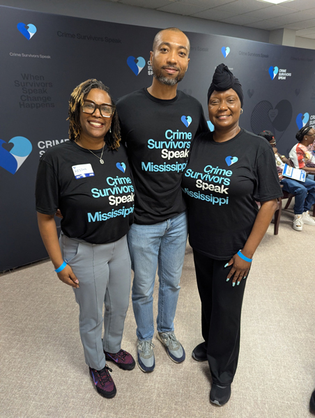 Three people standing close together for a group photo wearing matching black Crime Survivors Speak Mississippi shirts.